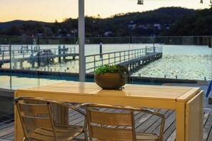 Una terraza de madera con una mesa y dos sillas, con vista a una masa de agua con un muelle y un embarcadero.