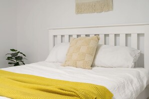 Una cama con cabecera blanca, dos almohadas blancas y una colcha amarilla.