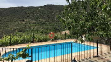 Una piscina con cerramiento de metal negro, rodeada de vegetación y colinas al fondo.