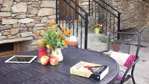 Uma casa de pedra com porta de madeira, escadaria e mesa redonda com livro e fruta.