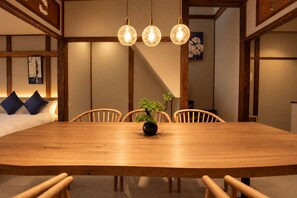 Ein Holzespeisesaal mit Stühlen, einem Blumentopf und hängenden Pendelleuchten in einem Raum mit Holzbalken und einem Bild an der Wand.
