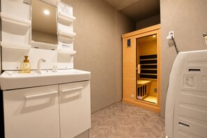 Ein Badezimmer mit Waschbecken, Spiegel und Holztür zur Sauna.