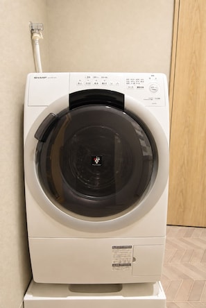 Eine Waschmaschine mit Frontlader, einer Bedienblende, einem Wasserzulaufschlauch und einem Warnhinweis.
