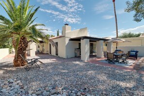 A patio area with a table and chairs, a palm tree, and a building with a white facade. - Extended Stay Gem: Tucson Townhome, Pool + Tennis (Tucson)