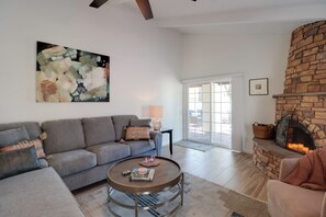 A modern living room with a grey sofa, a round wooden coffee table, and a stone fireplace. - Extended Stay Gem: Tucson Townhome, Pool + Tennis (Tucson)
