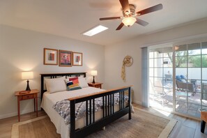 A bedroom with a bed, two bedside tables, a ceiling fan, and a large window with a view of the outdoors. - Extended Stay Gem: Tucson Townhome, Pool + Tennis (Tucson)