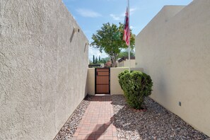 A narrow pathway leading to a gated entrance with a flagpole. - Extended Stay Gem: Tucson Townhome, Pool + Tennis (Tucson)