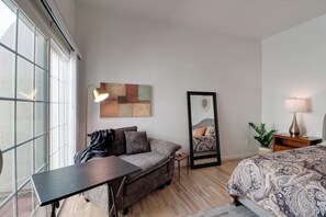 A modern bedroom with a large window, a sofa, a bed, a desk, and a nightstand with a lamp. - Extended Stay Gem: Tucson Townhome, Pool + Tennis (Tucson)