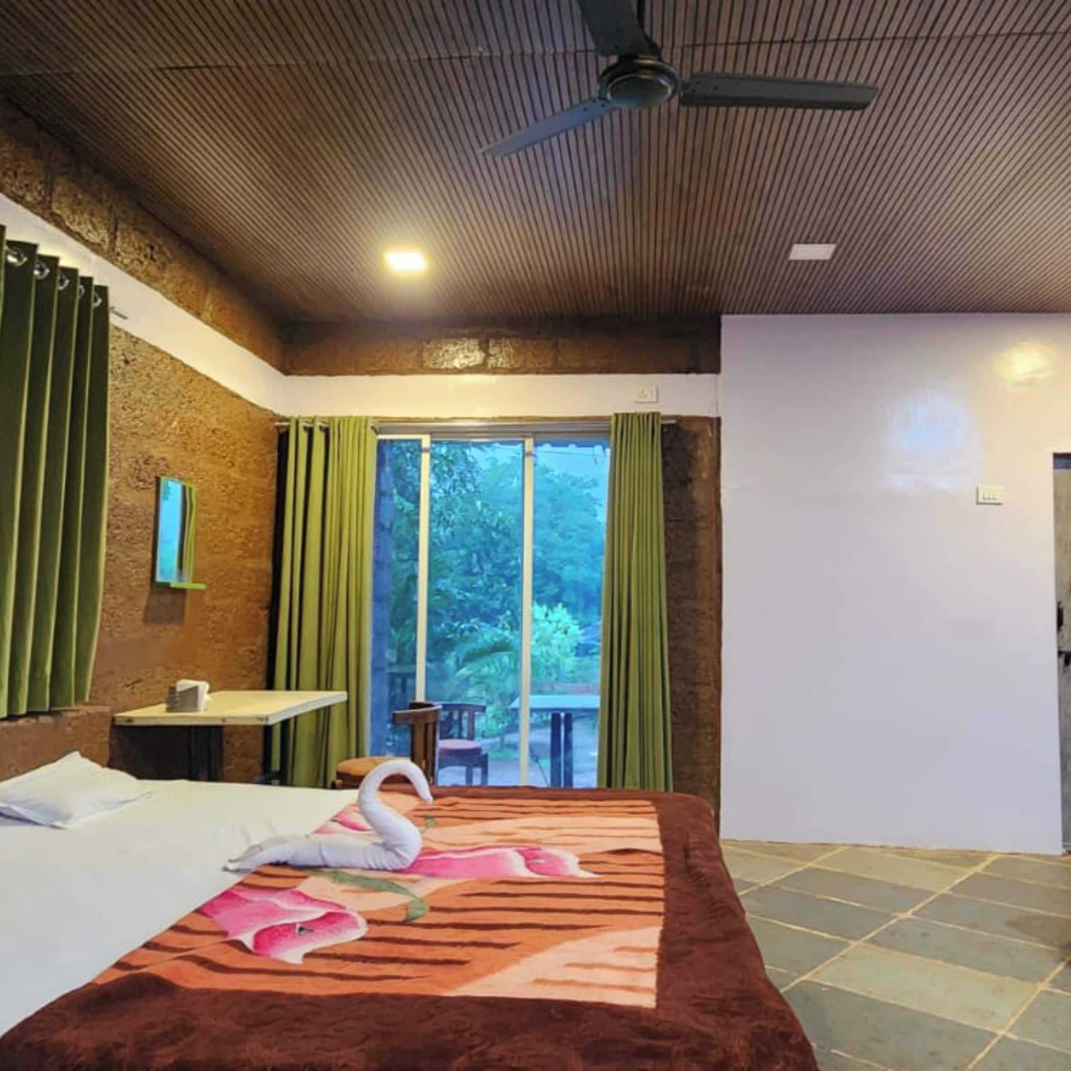 A hotel room with a bed, a table, a chair, a ceiling fan, and a view of the outdoors.