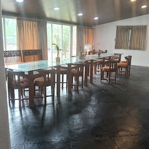 Una habitación amplia con una gran mesa de vidrio rodeada de sillas de madera, un banco y una planta en maceta.