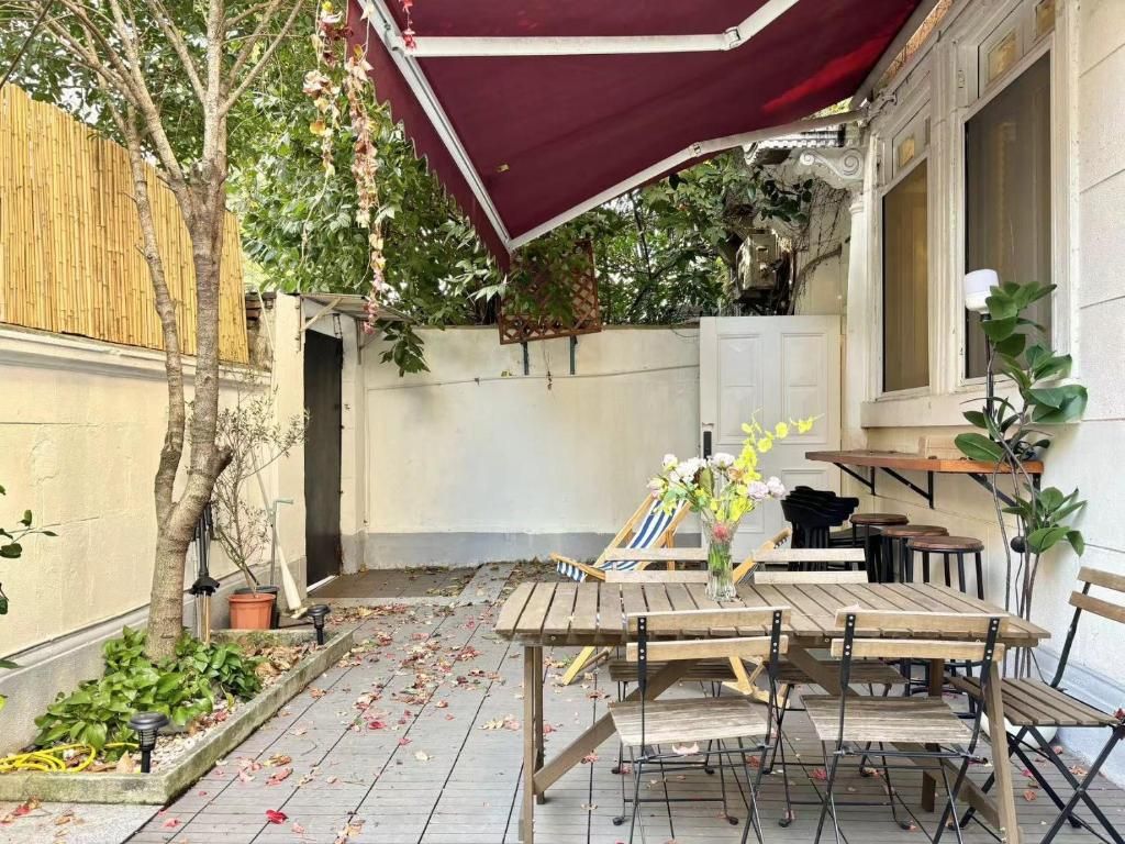 An outdoor patio with a wooden table and chairs, a red canopy, and potted plants.