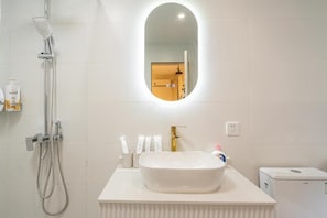 Een badkamer met een wit wastafel, een handdouche en een spiegel aan de muur.