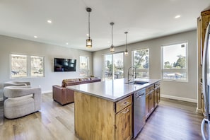 A modern kitchen with a large island, wooden cabinets, and pendant lighting.