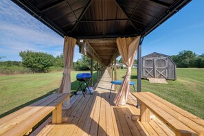 An outdoor covered patio with wooden benches and a grill.