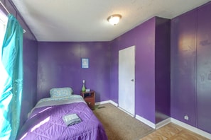 A bedroom with purple walls, a bed with a floral duvet, a nightstand with a lamp, and a door.