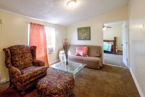 A living room with a floral armchair, a glass coffee table, a sofa, and a painting on the wall.