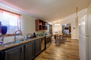 A kitchen with a central island, dark cabinetry, a stainless steel sink, and a dining area with a table and chairs.