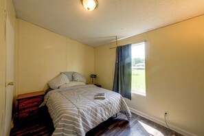 Ein Schlafzimmer mit einem Bett, einem Nachttisch, einem Fenster mit Vorhängen und einer Tür.