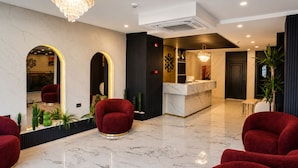 Un hall d’entrée moderne avec un sol en marbre, des fauteuils à revêtement rouge, un comptoir d’accueil et un lustre.