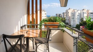 Un balcon avec une table et des chaises, donnant sur un paysage urbain avec des bâtiments et un ciel dégagé.