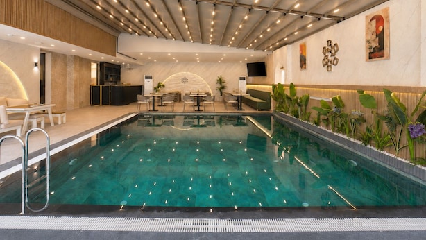 Une piscine intérieure dotée d’un plafond composé de poutres parallèles et d’un éclairage encastré, entourée d’espaces de détente et d’un comptoir d’accueil.