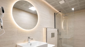 Une salle de bain moderne avec un grand miroir ovale, un lavabo blanc et une douche à parois de verre.