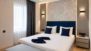 Une chambre d’hôtel avec un grand lit, une table de chevet, une commode, un mur orné de panneaux décoratifs et une fenêtre avec des rideaux.