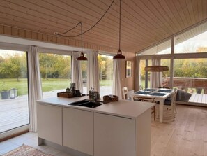 A modern kitchen with a large island, a dining area with a table and chairs, and a view of a garden through large windows. - 4 Star Holiday Home in Vejby (Vejby)
