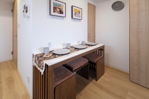 A dining area with a wooden table, two chairs, a clock, and two framed pictures on the wall. - JY Suites Namba (Nipponbashihigashi, Naniwa Ward)