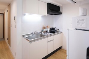 A compact kitchen with a stainless steel sink, a black range hood, and a white refrigerator. - JY Suites Namba (Nipponbashihigashi, Naniwa Ward)