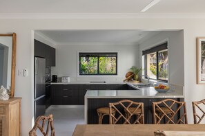 Une cuisine moderne avec des meubles de couleur sombre, un réfrigérateur en acier inoxydable, un grille-pain et une fenêtre donnant sur un paysage verdoyant.