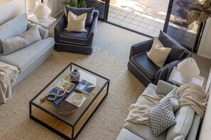 Un salon moderne avec une table basse en verre, des canapés et une vue sur l’extérieur.
