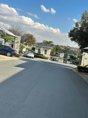 A street view with parked cars, a building with a satellite dish, and a clear sky. - Modern Fourways -Spacious 3Bedroom Retreat& 2 bath (Sandton)