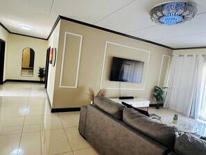 A modern living room with a flat-screen TV, a sofa, and a dining area with a small table. - Modern Fourways -Spacious 3Bedroom Retreat& 2 bath (Sandton)