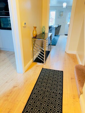 A hallway with a black patterned rug, a glass table with a vase, and a sofa in the background. - More photos to come in few weeks (Reedham)