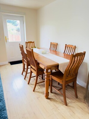 A dining room with a wooden table and chairs, a white door, and a view of the outside. - More photos to come in few weeks (Reedham)