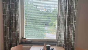 A room with a table, two chairs, a hanging light fixture, a window with blinds, and a radiator. - Cozy 2-Bedroom Apartment in Central Rågsved, Stockholm (Bandhagen)