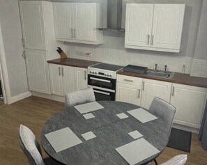 A compact kitchen with white cabinets, a stove, and a sink. There is a round table with chairs. - 2 Bedroom Villa, Sleeps 5, WiFi, Parking, Beach (Dawlish Warren)