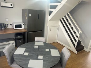A compact kitchen with a refrigerator, microwave, and kettle, a dining table with chairs, and a staircase. - 2 Bedroom Villa, Sleeps 5, WiFi, Parking, Beach (Dawlish Warren)