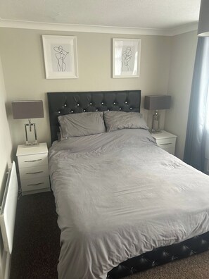 A neatly made bed with a tufted headboard, two bedside tables with lamps, and two framed abstract artworks on the wall. - 2 Bedroom Villa, Sleeps 5, WiFi, Parking, Beach (Dawlish Warren)