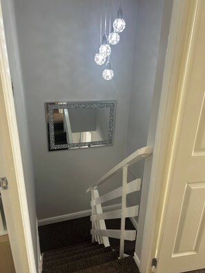 Ein Flur mit einem Spiegel an der Wand, einer Treppe mit weißer Geländer und dekorativen Lampen an der Decke.