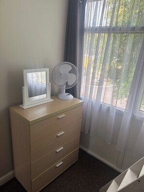 A room with a wooden dresser, a white fan, and a window with sheer curtains. - 2 Bedroom Villa, Sleeps 5, WiFi, Parking, Beach (Dawlish Warren)