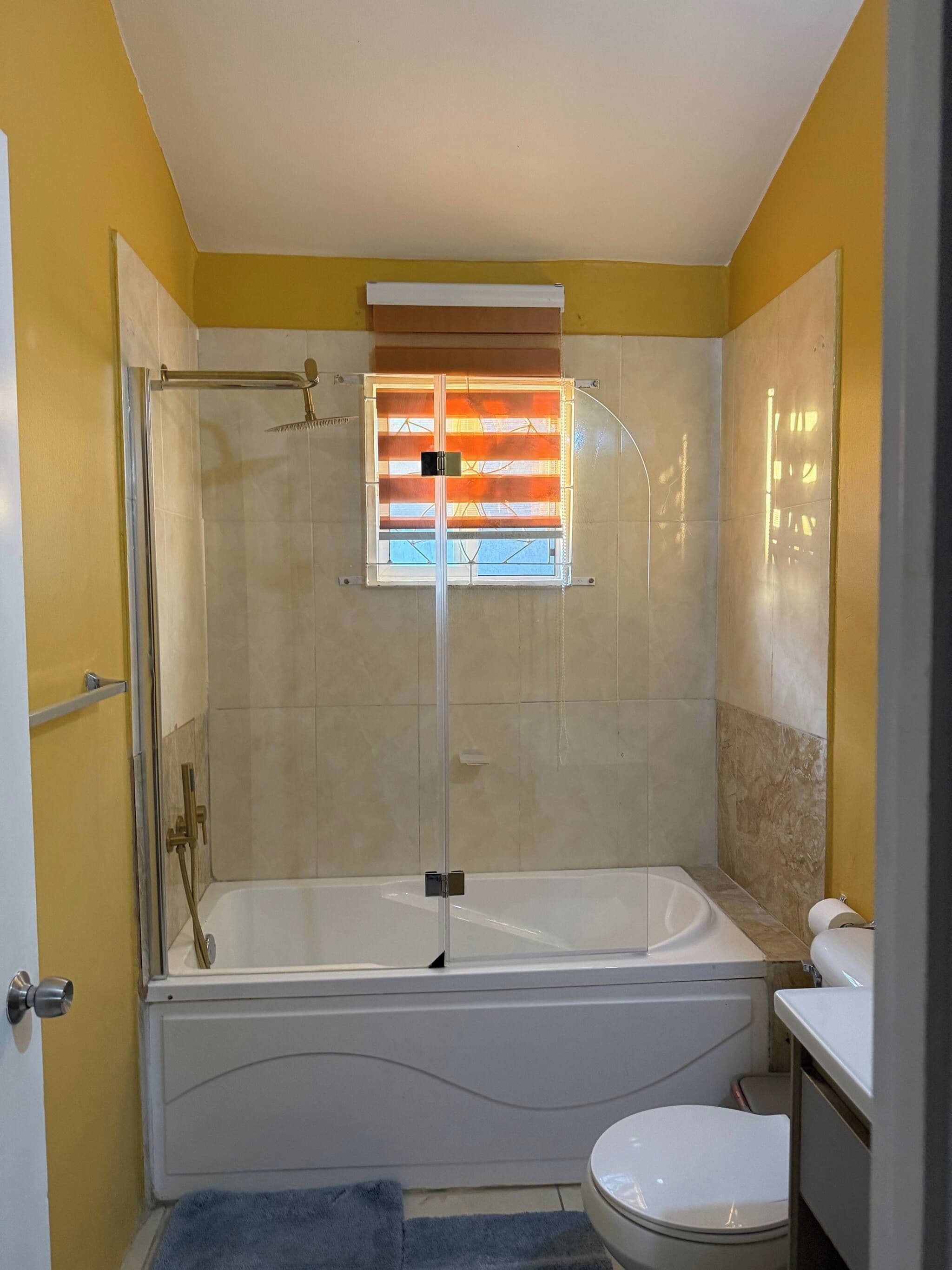 Un baño con bañera, inodoro y ventana con persianas.