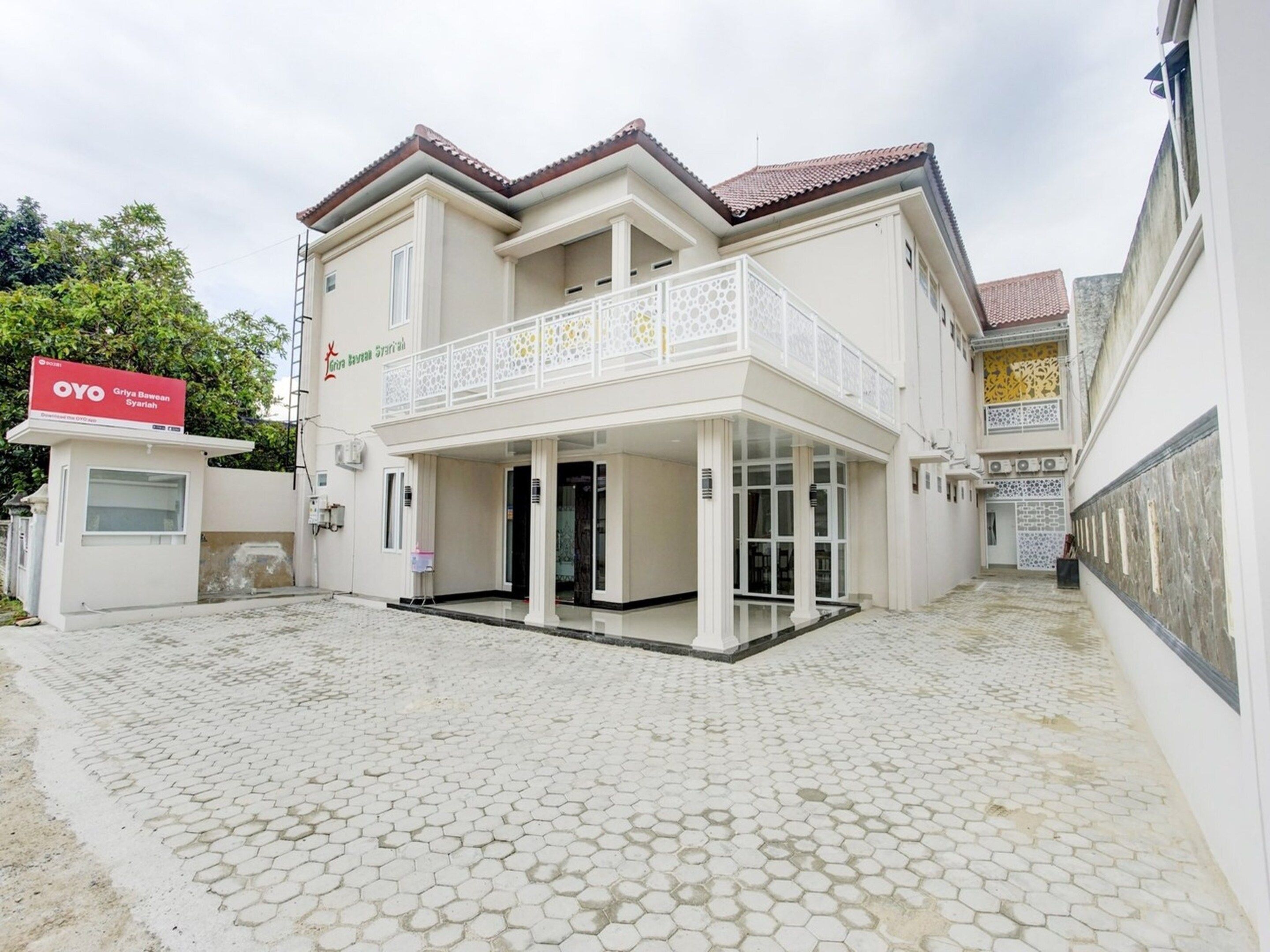 A two-story building with a balcony, a covered entrance, and a tiled courtyard.
