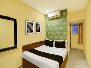 A hotel room with a bed, two framed leaf patterns on the wall, an air conditioning unit, and a window with curtains. - Premium James Street Railway Station Hyderabad (Hyderabad)