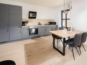A modern kitchen with grey cabinets, a wooden dining table, and a black chair. - Coastal Suite North Directly on the Waterfront (Krummhoern)