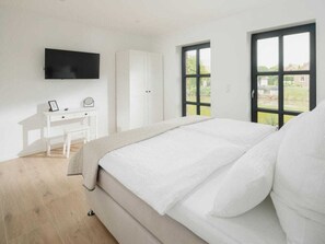 A bedroom with a bed, a desk, a chair, a wardrobe, and a TV mounted on the wall. - Coastal Suite North Directly on the Waterfront (Krummhoern)