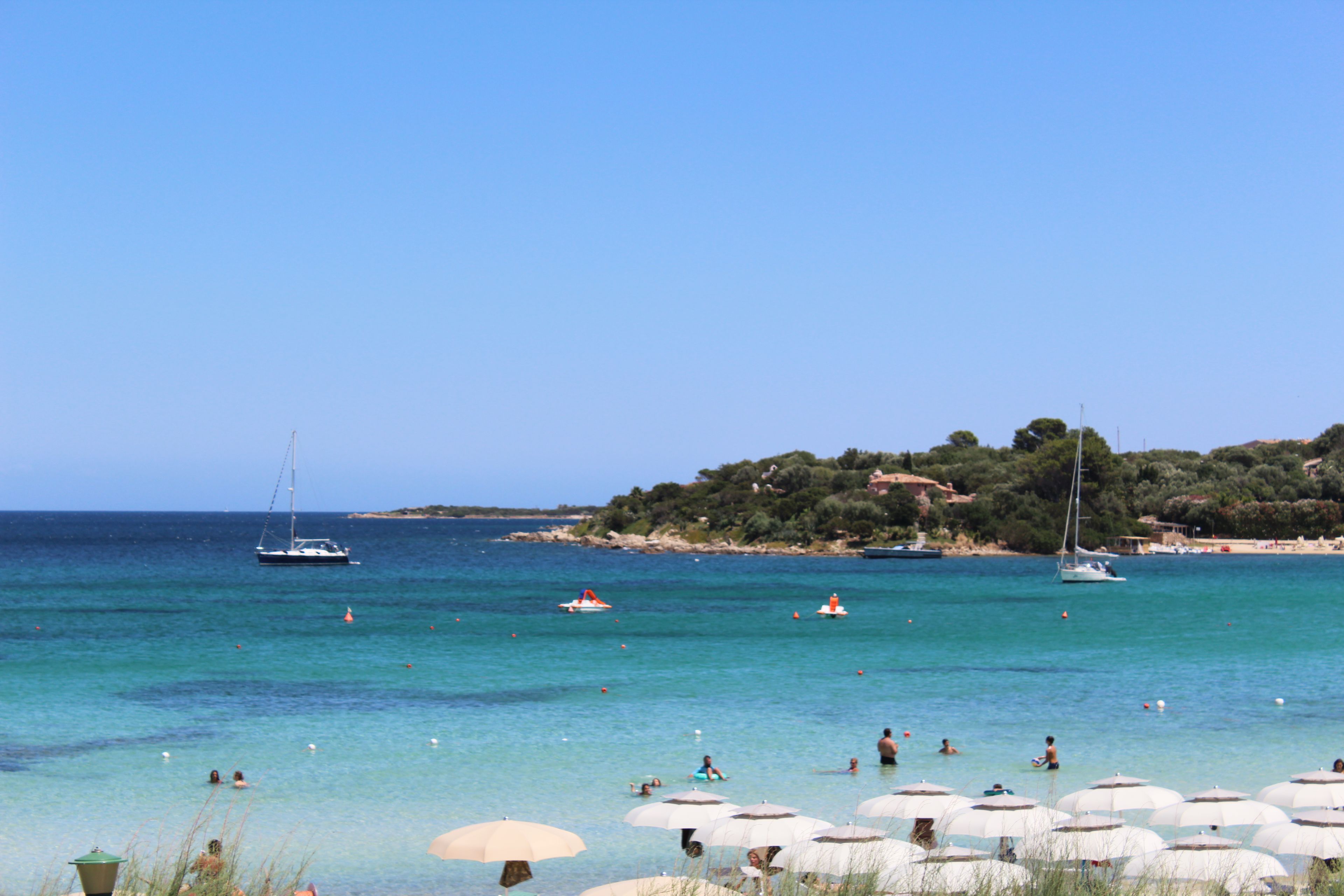 Una spiaggia con acque cristalline, ombrelloni e barche.