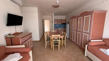 Een compact woongedeelte met een kitchenette, een eethoek en een aan de muur bevestigde televisie.