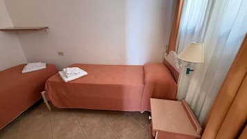 Een kleine, eenvoudige kamer met twee enkele bedden, een klein houten nachtkastje en een lamp aan de muur.